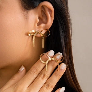 Close-up of golden bow earrings with snake chain texture on model ear