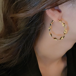 Detail of gold twisted hoop earrings with spiral texture and glossy metallic finish