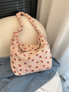 Pink corduroy shoulder bag with sweet strawberry print and pleated strap on a soft chair
