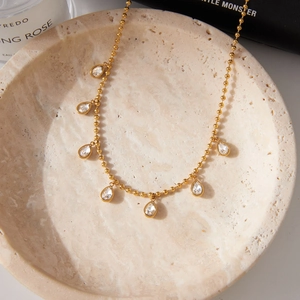 Classic gold beaded necklace with seven teardrop zircon pendants on a marble tray