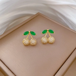 Detailed macro view of cherry stud earrings with green crystal leaves and white micro-pave