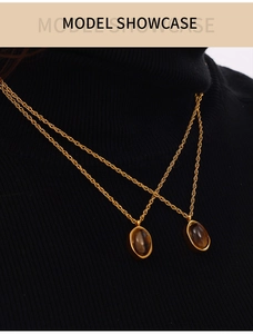 Détail du pendentif en oeil de tigre sur une chaîne dorée torsadée sur pull noir