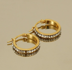 Macro view of gold hoop earrings with sparkling white crystals on a mirror surface