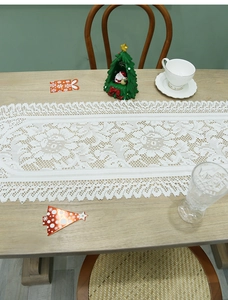 Detailed white lace table runner with hollow floral patterns and fringed edges on wood