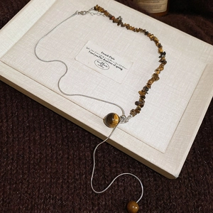 Detail of silver snake chain necklace with tiger eye stone beads on a textured tray