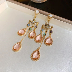 Detailed macro view of pink crystal teardrop earrings with gold tassel and star accents