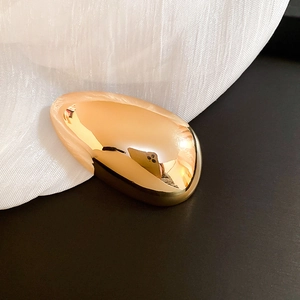Macro shot of minimalist polished gold oval brooch with reflective mirror finish