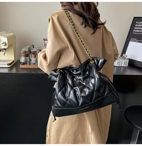 Detail of black quilted chain shoulder bag with glossy finish and brand lettering