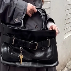 Minimalist black leather tote bag with belt buckle and key charm shown outdoors