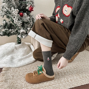 Dettaglio di calze natalizie grigie ricamate con pantaloni di velluto e scarpe foderate