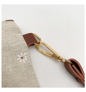 Detail of a straw woven envelope bag featuring white daisy prints and brown leather strap