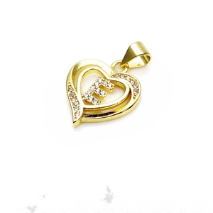Macro shot of a gold heart pendant with cubic zirconia and the letter F on white background