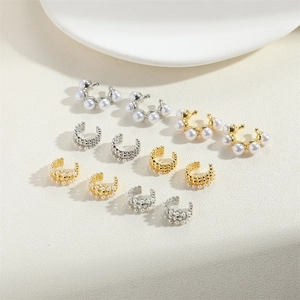 Macro shot of assorted gold and silver pearl ear cuffs set against a beige ceramic dish