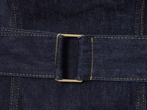 Gros plan d'une boucle dorée rectangulaire sur un denim bleu marine à coutures jaunes