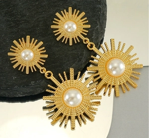 Détail de boucle d'oreille soleil dorée avec perle sur fond de pierre noire texturée