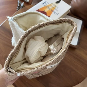 Detailed interior of tweed cosmetic bag showing beige fabric lining and storage capacity