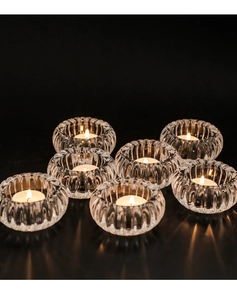 Vue détaillée de 7 photophores en verre nervuré avec des bougies allumées sur fond sombre
