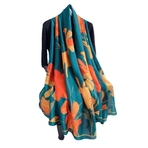 Elegant dark green silk scarf with large orange and yellow floral prints on mannequin