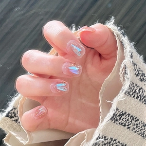 Close-up of round nude blush press-on nails with iridescent butterfly and gold glitter