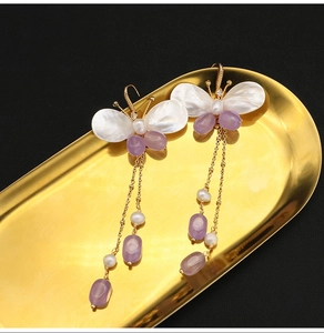 Detailed shot of butterfly tassel earrings with purple beads and pearls in a gold tray