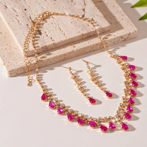 Detail shot of golden necklace and earrings set with pink drop-shaped gemstones and crystals