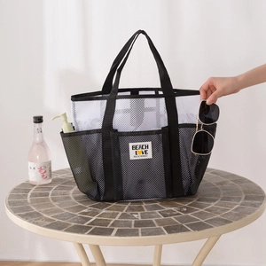 Large mesh beach tote bag with exterior pockets and Beach Love label on a stone table
