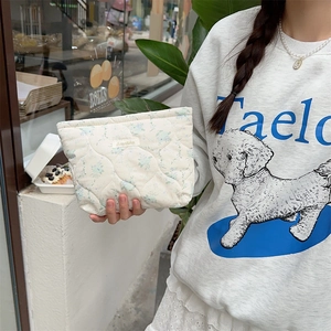 Detail of white quilted cotton makeup bag with blue floral print held by a model