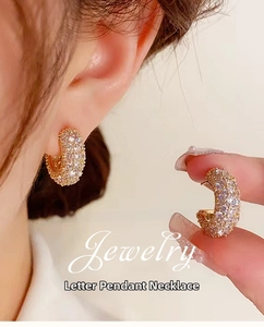 Close-up of gold-plated C-shaped hoop earrings with shimmering pavé zircon stones