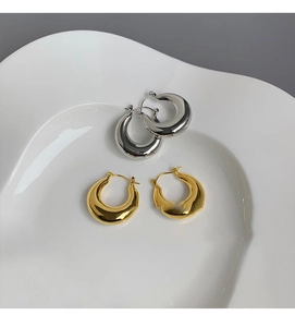 Gros plan de boucles d'oreilles créoles dorées et argentées sur un plateau en céramique