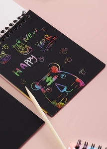 Rainbow DIY scratch art notebook with wooden stylus on a pink background