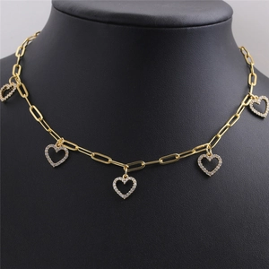 Gros plan sur collier chaîne trombone doré avec pendentifs cœur brillants sur support