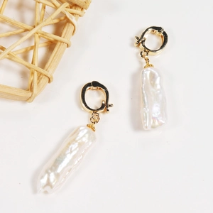 Detailed view of baroque pearl gold hoop earrings on a minimalist white background