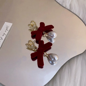 Detail of red flocked bow earrings with golden heart studs and teardrop pearls on a mirror