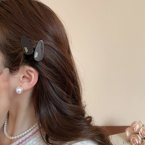 Détail de barrettes en acrylique noir brillant avec lettrage doré sur un mannequin élégant
