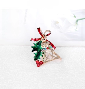 Detailed close-up of a Christmas bell brooch with green holly leaves and red rhinestones