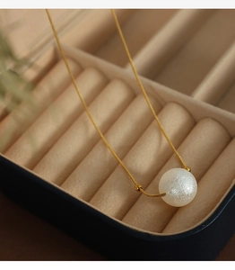 Detailed shot of golden double-layer necklace with large white pearl in a beige jewelry box
