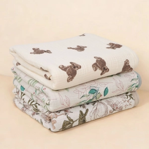 Three stacked cotton muslin baby swaddle blankets with cute bear and floral patterns