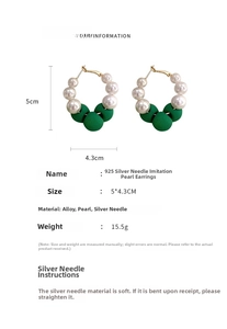 Macro detail of C-shaped earrings with white pearls and green textured beads on gold alloy