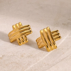 Macro shot of polished gold-finished cross-striped stud earrings on textured sandstone