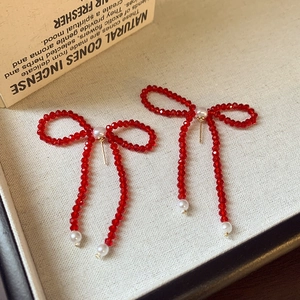 Dettaglio di orecchini a fiocco con perline rosse e perle bianche su carta vintage