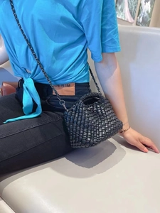 Close-up of black woven leather bucket bag with chain strap held by a seated model
