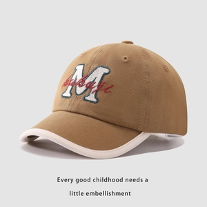 Dettaglio di un cappellino da baseball marrone per bambini con ricamo M e bordo bianco