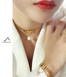 Detail showing gold stainless steel mesh jewelry set with letter M and white pearls