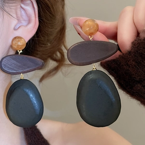 Close-up of geometric earrings with amber bead, wood oval, and dark pebble pendant