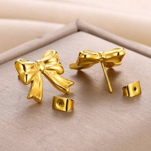 Detailed close-up of polished 18K gold bow-shaped stud earrings on a beige velvet stand