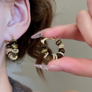 Detail of golden hoop earrings with tiger eye beads shown on a model's ear lobe