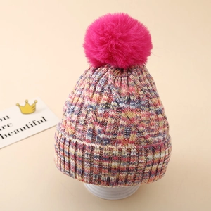Nahaufnahme der groben Zopfstrickstruktur am bunten Winterhut mit großem rosa Bommel