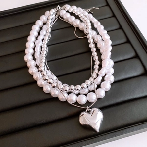 Macro shot of multi-layer pearl necklace featuring a silver heart pendant on black display