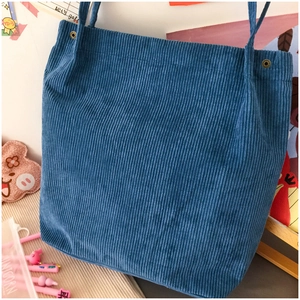 Blue corduroy tote bag detail showing metal rivets and soft fabric texture on a desk