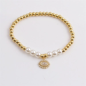 Elegant gold bead and pearl evil eye pendant bracelet with crystal accents on a grey base